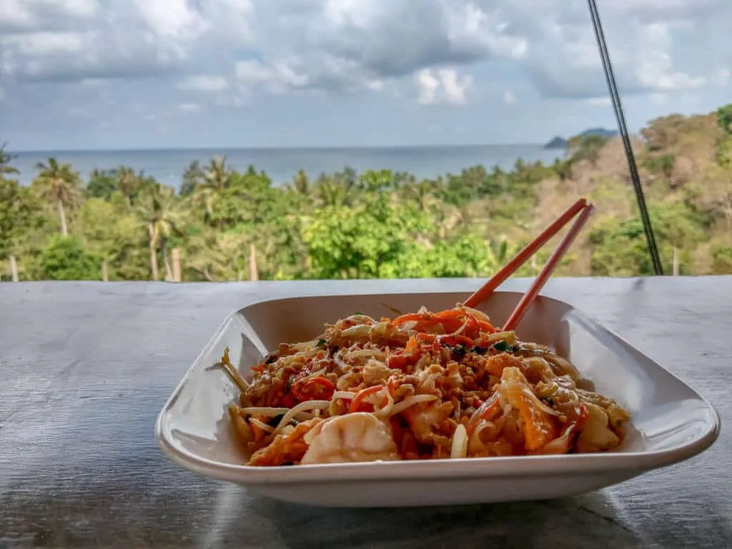 Miska makaronu pad thai z krewetkami i pałeczkami na tle tropikalnego wybrzeża